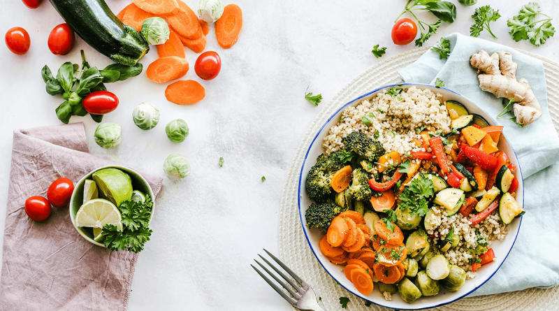 A vibrant and colorful salad made of carrot slices, cherry tomatoes, broccoli, squash, brussels sprouts and couscous.