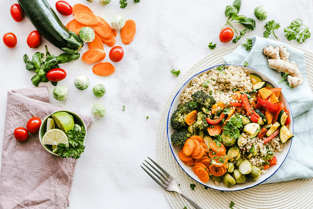 A vibrant and colorful salad made of carrot slices, cherry tomatoes, broccoli, squash, brussels sprouts and couscous.