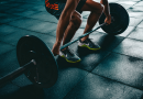 A person preparing to lift a barbell with large weights. Only their arms and legs are visible as they grip the barbell.