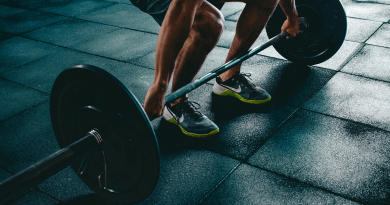 A person preparing to lift a barbell with large weights. Only their arms and legs are visible as they grip the barbell.