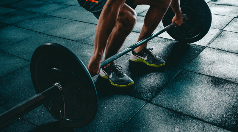 A person preparing to lift a barbell with large weights. Only their arms and legs are visible as they grip the barbell.