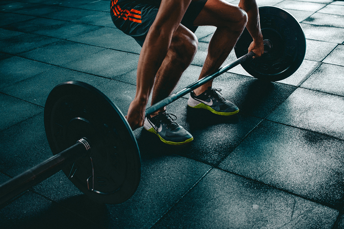 A person preparing to lift a barbell with large weights. Only their arms and legs are visible as they grip the barbell.