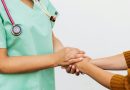 A person wearing light green scrubs holding another person's hands. Both are seen from the neck down.