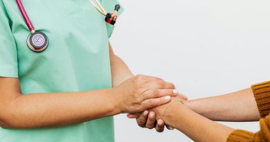 A person wearing light green scrubs holding another person's hands. Both are seen from the neck down.