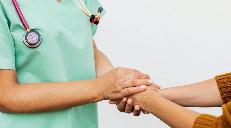 A person wearing light green scrubs holding another person's hands. Both are seen from the neck down.