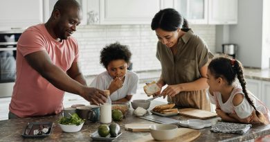 A family in the kitchen putting together a meal, with bowls of cereal, avocados and slices of toast.