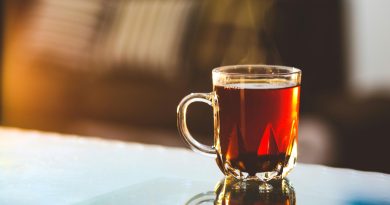 A glass mug of caramel-colored tea steams on table.