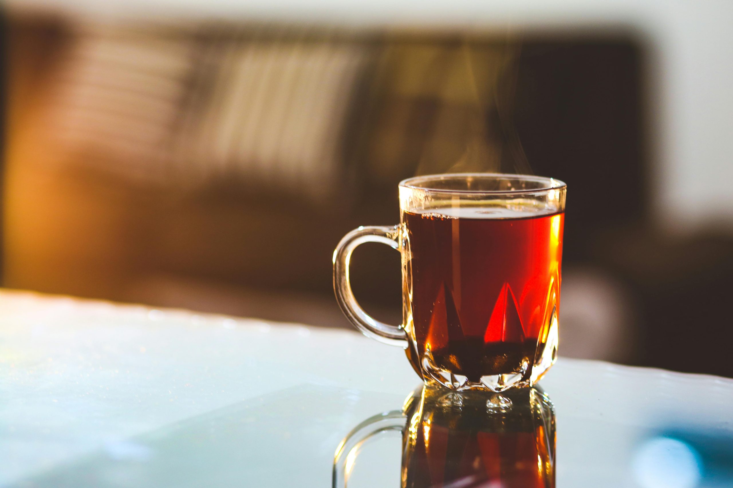 A glass mug of caramel-colored tea steams on table.