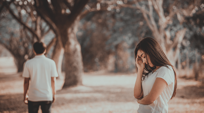 A person walking away from another person, who is holding their head and looking sad.