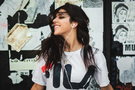 Woman listening to music with earphones in front of a wall with posters on it.