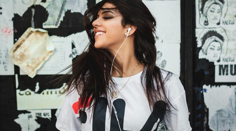 Woman listening to music with earphones in front of a wall with posters on it.