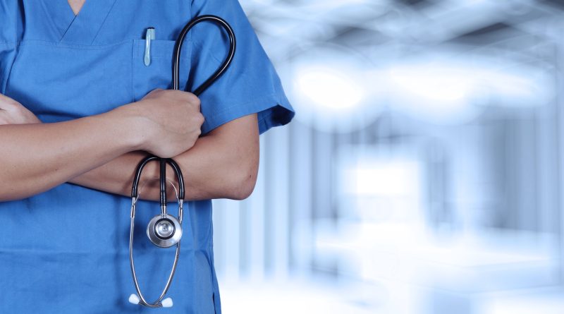 Doctor in scrubs holding stethoscope.