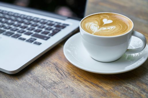 Cup of coffee next to a laptop.