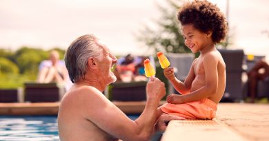 Grandfather and grandson eating popsicles at edge of swimming pool