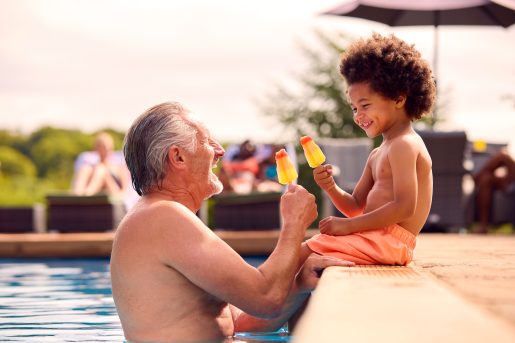 Grandfather and grandson eating popsicles at edge of swimming pool