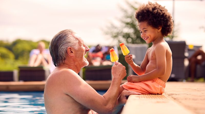 Grandfather and grandson eating popsicles at edge of swimming pool