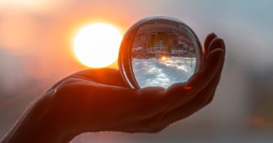 Sun and glass ball in hand, man holding crystal ball, crystal lens with sun rays and city as reflection