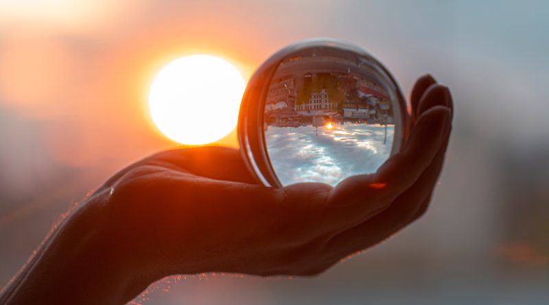 Sun and glass ball in hand, man holding crystal ball, crystal lens with sun rays and city as reflection