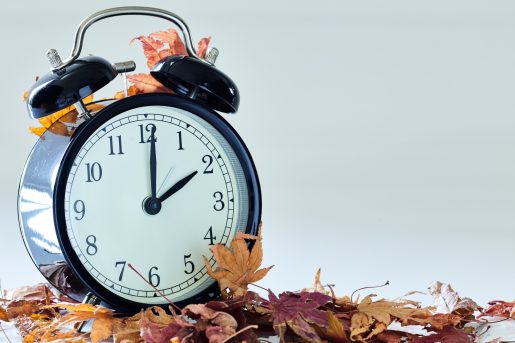 Image of autumn Time Change, Fall back concept, Dry leaves and vintage alarm Black Clock on wooden table outdoors at afternoon