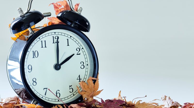 Image of autumn Time Change, Fall back concept, Dry leaves and vintage alarm Black Clock on wooden table outdoors at afternoon