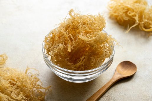 Close up of golden dried Sea Moss in a clear bowl with a wooden spoon.