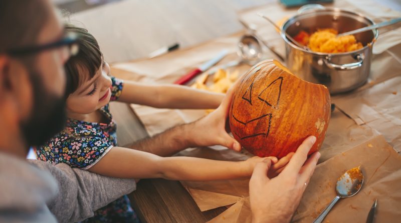 Little girl and her father holding a Halloween pumpkin. Family spending time together.