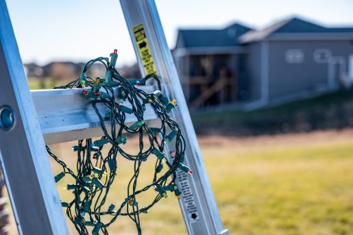 Prep for installing Christmas lights by leaning a ladder against a house and setting out lights