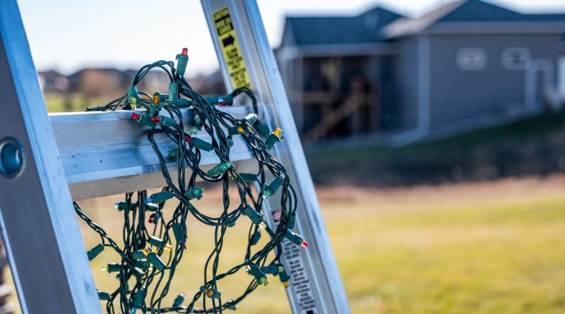 Prep for installing Christmas lights by leaning a ladder against a house and setting out lights
