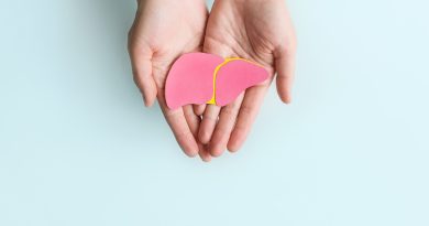 Two hands gently holding a pink anatomical model of a human liver with a yellow outline, against a light blue background