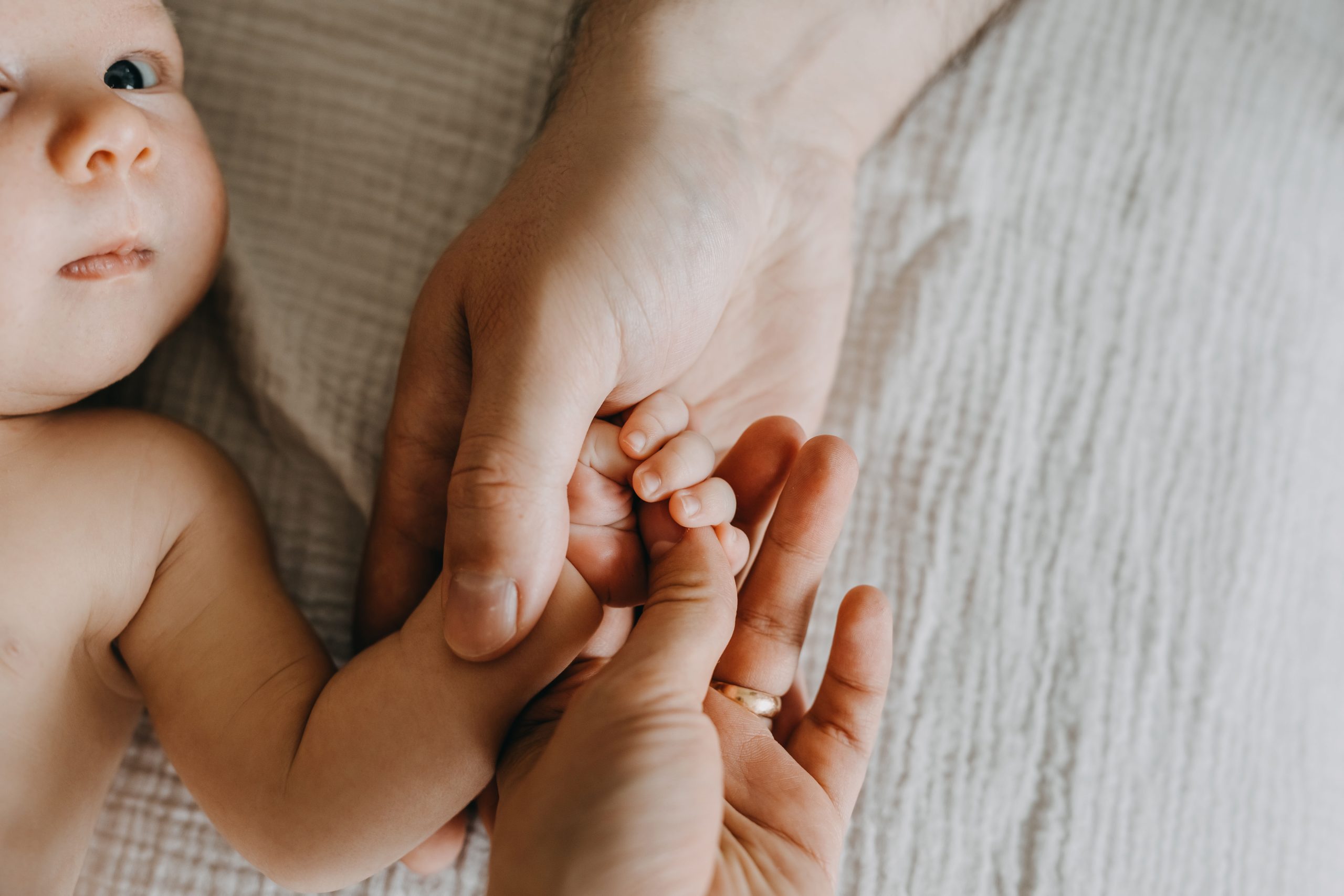 Parents holding newborn baby hand.