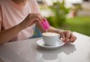 Woman pouring sugar packet into coffee.