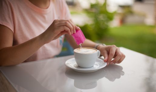 Woman pouring sugar packet into coffee.