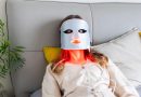 Woman using LED light therapy mask at home. Relaxing on couch.