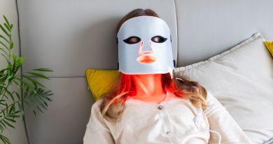 Woman using LED light therapy mask at home. Relaxing on couch.