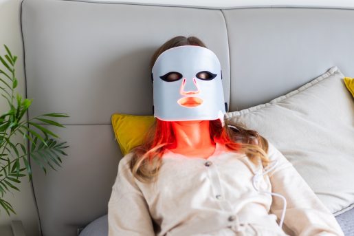 Woman using LED light therapy mask at home. Relaxing on couch.