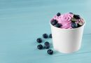 Cup with tasty frozen yogurt and blueberries on blue wooden table.