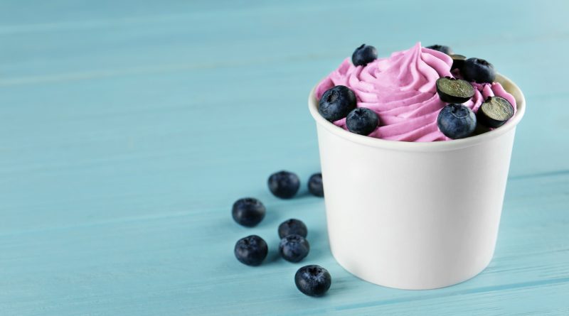 Cup with tasty frozen yogurt and blueberries on blue wooden table.