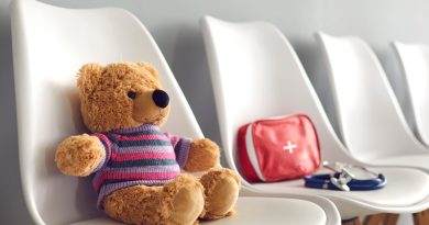 First-aid kit, stethoscope and cute teddy bear on white chairs in waiting room of children's medical center or pediatric clinic. Concept of kids' visit to hospital to see pediatrician or family doctor.
